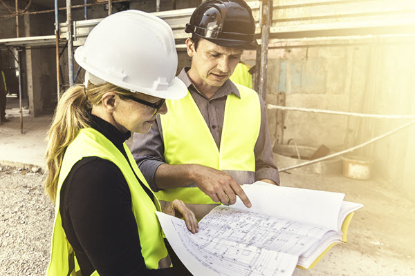 Image of man and woman in hard hats and high-vis vests looking at plans on a construction site
