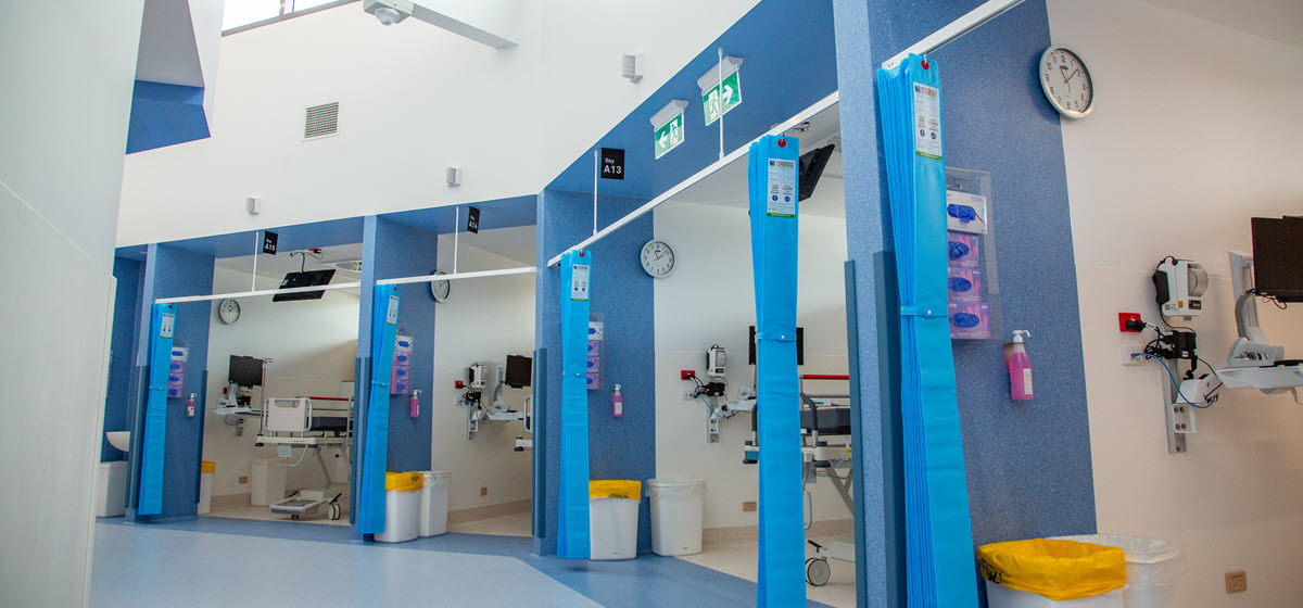 A row of cubicles in an emergency department, with blue walls and blue curtains