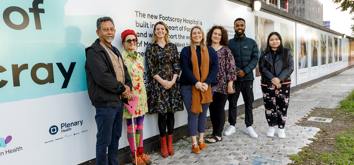 Group of people standing in front of the new Faces of Footscray exhibition on the hoarding of the hospital site on the corner of Geelong Road and Federal Street. 