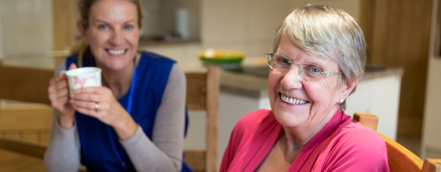 An older woman and carer smile at the camera