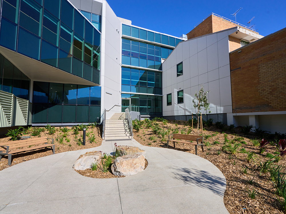 Landscaped hospital courtyard with seating, native planting and a modern building facade