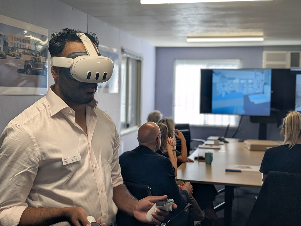 A Barwon Health staff member uses a virtual reality headset to view the Barwon Women's and Children's design, with colleagues watching on a screen nearby.