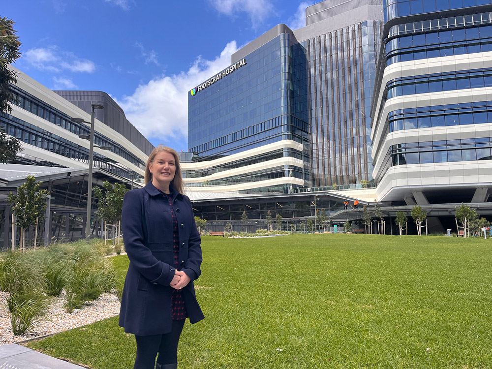 A women smiles at the camera while standing in a green outdoor space