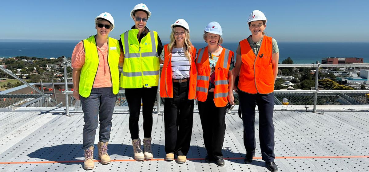 A group of people stand proudly in hard hats and hi-vis vests up high on a construction site