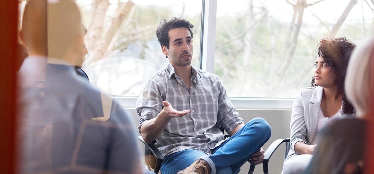 A man in a check shirt gestures and speaks in a circle of people