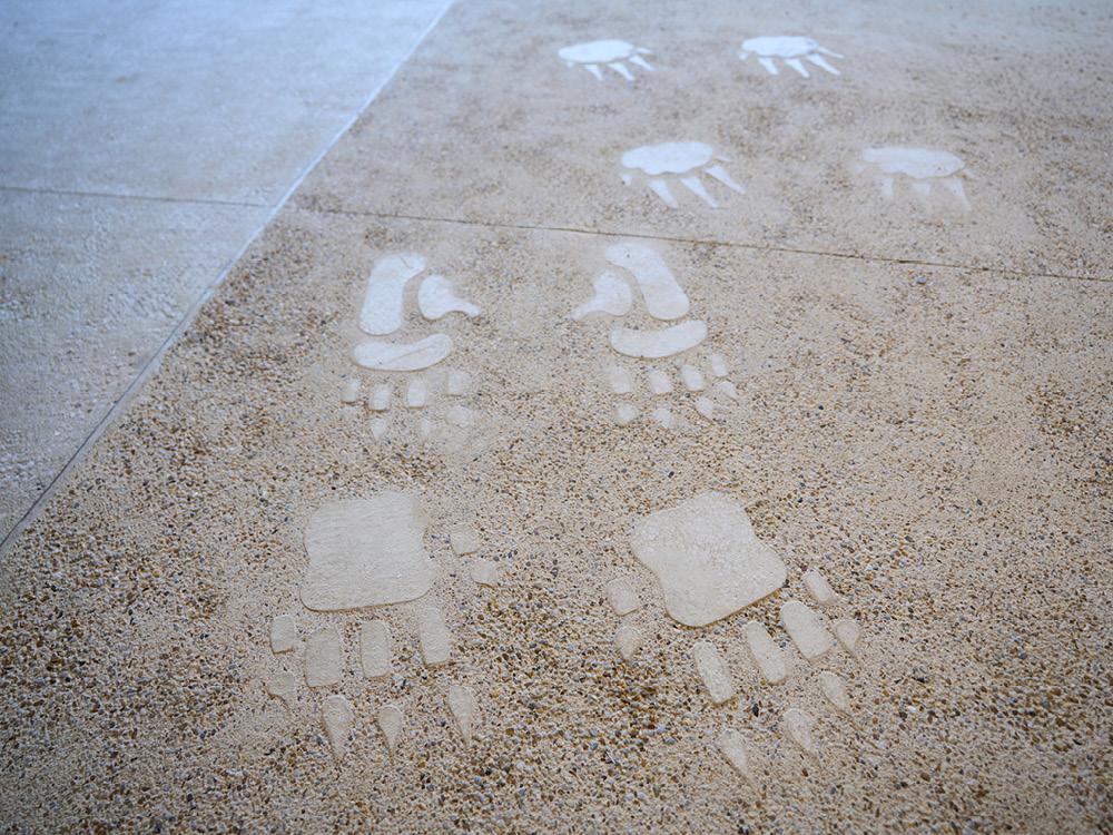 Footprint and track motifs embedded in a textured floor surface as part of an Indigenous wayfinding design.