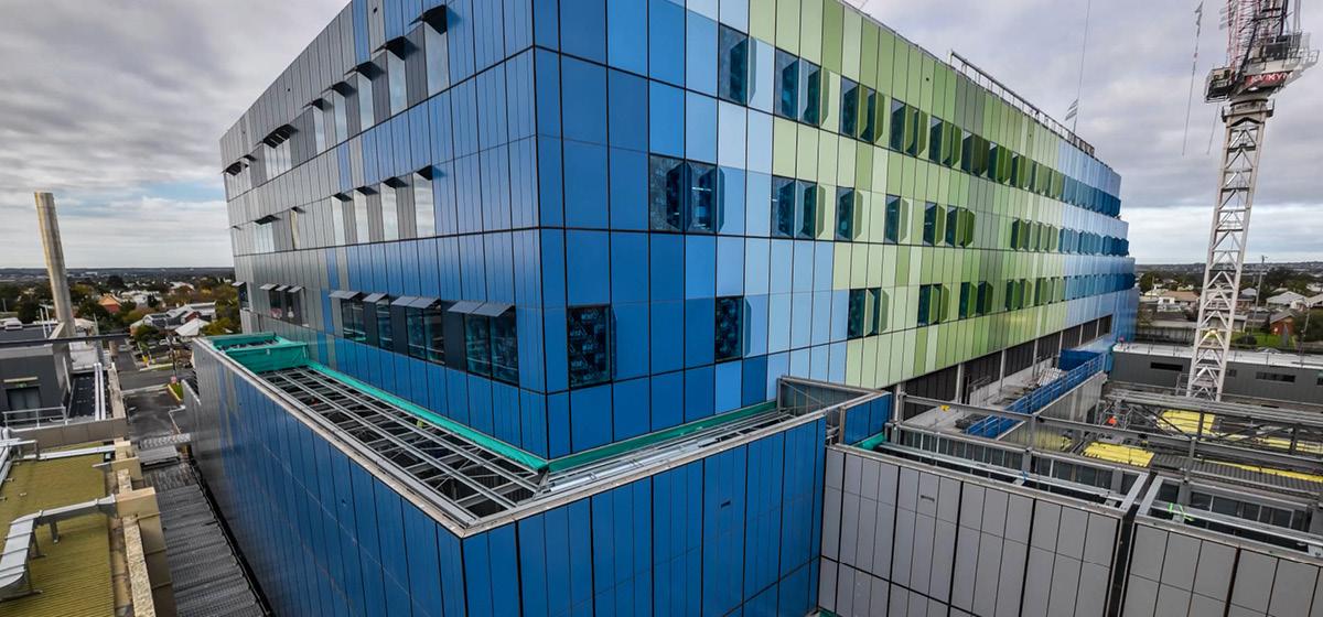 Close-up view of the Barwon Women's and Children's building under construction, showing the blue and green glass exterior and a tower crane.