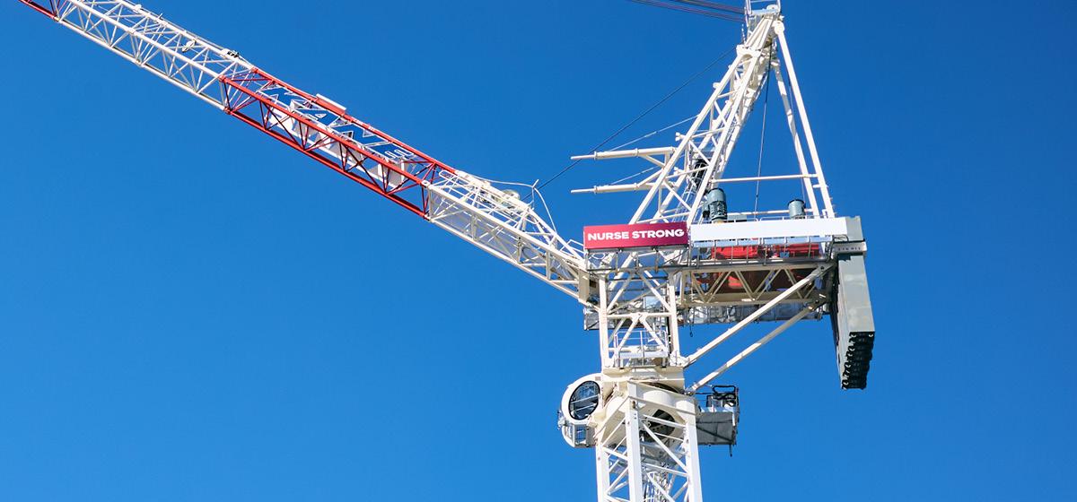 A crane against a blue sky with signage that says 'Nurse Strong'