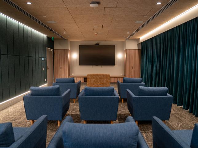 A room with a wall-mounted television and many padded chairs