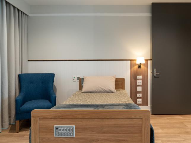A bedroom with a single bed, padded chair and wall-mounted lamp