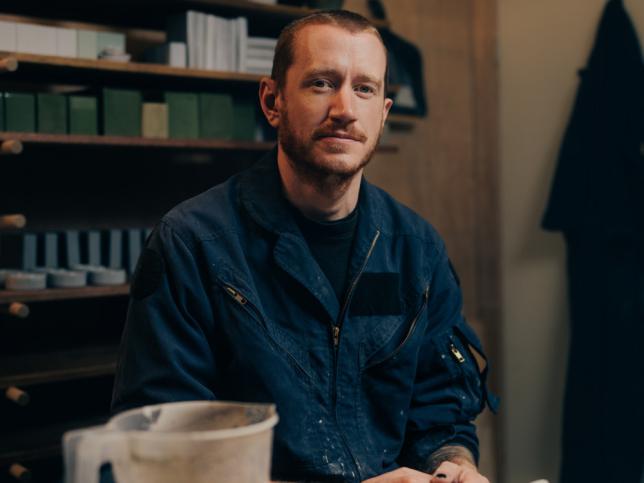 A man sits in a sculpting studio and looks at the camera