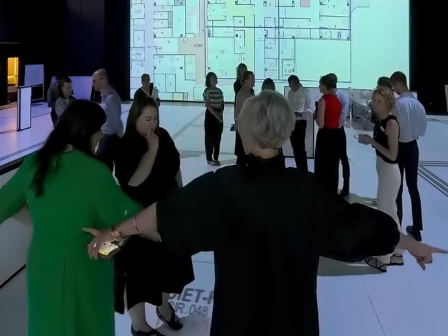 A group of people standing in an open indoor space, looking at plans projected onto the floor
