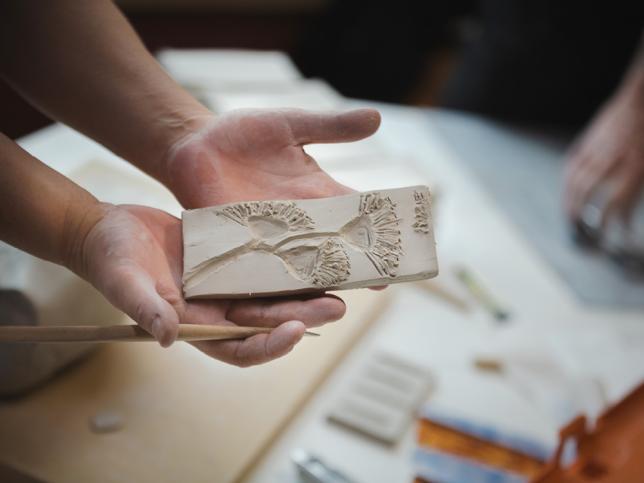 A pair of hands holding a clay piece with a flower etched into it