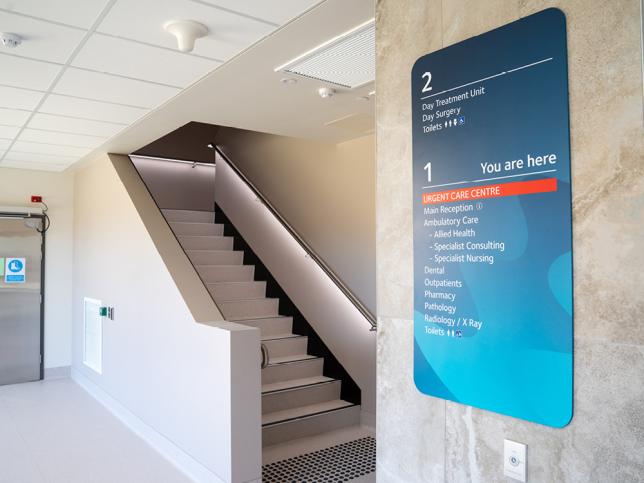 A set of stairs inside the Phillip Island Community Hospital, with a sign listing services on Floors 1 and 2