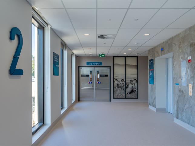 A walkway on the second floor of the Phillip Island Community Hospital, with a lift to the right and doors to Day Surgery ahead