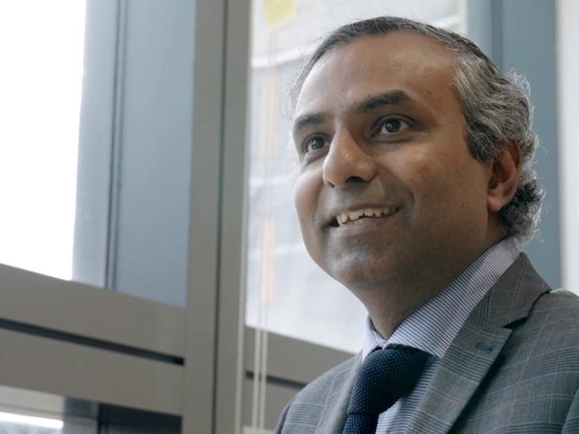 A man in a suit and tie smiles just past the camera