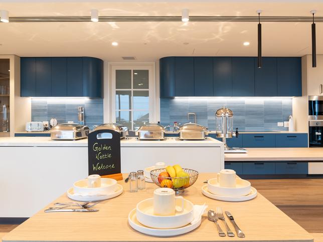 Dining table with set plates and cutlery in the foreground, with a kitchen area in the background.