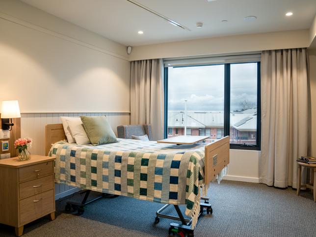 Bedroom at the new aged care facility, with a bed, bedside table and window in the background.