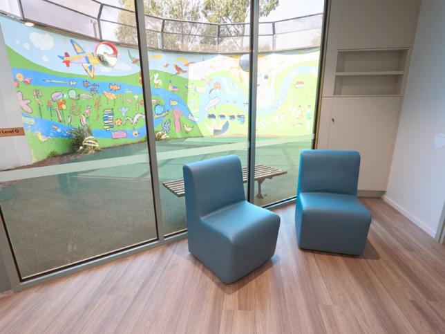 Two blue chairs in front of a large glass window overlooking a colourful courtyard mural.