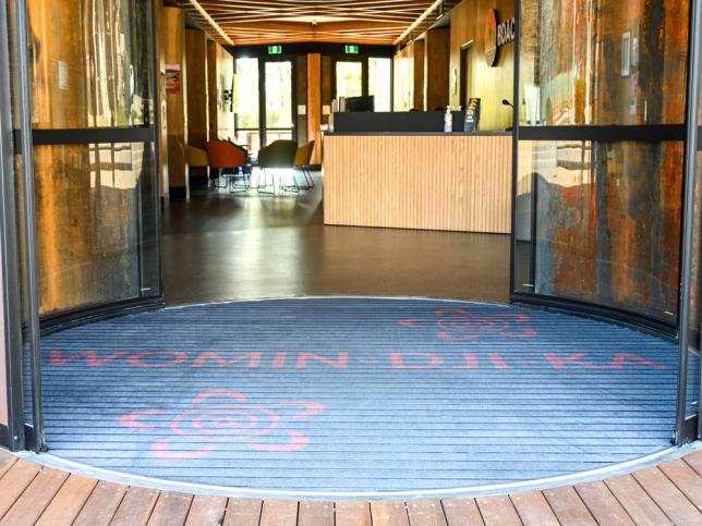 Circular blue entrance mat at the reception area of a modern building, with glass doors open.