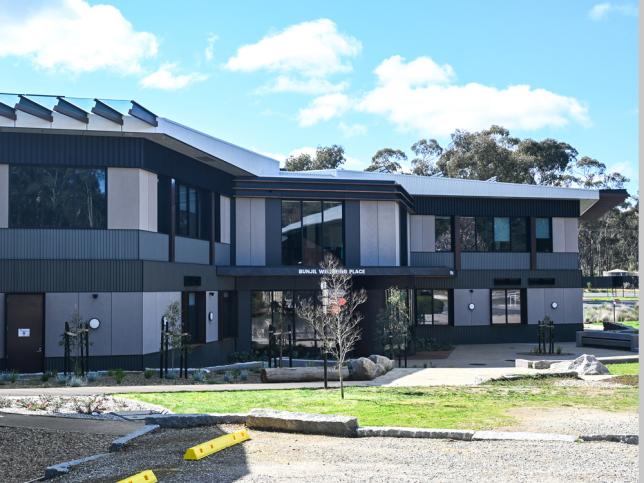Front view of a building under bright daylight, featuring modern architecture with large glass windows and landscaped front area.