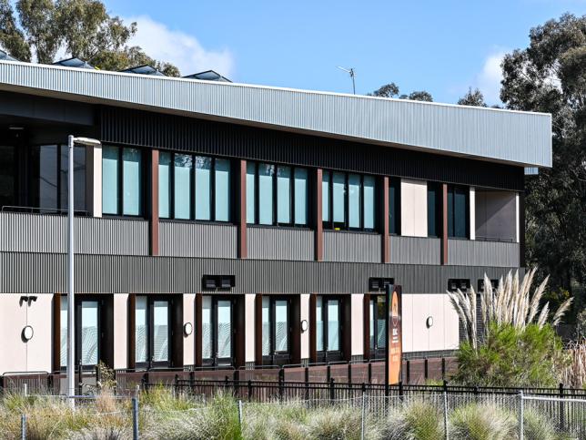 Exterior view of the a modern building featuring large windows and dark cladding, surrounded by natural vegetation.