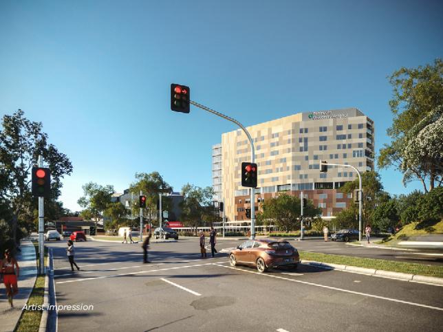 Artist impression of a busy intersection with red traffic lights, featuring pedestrians crossing, a car in the foreground, and a large modern hospital in the background.