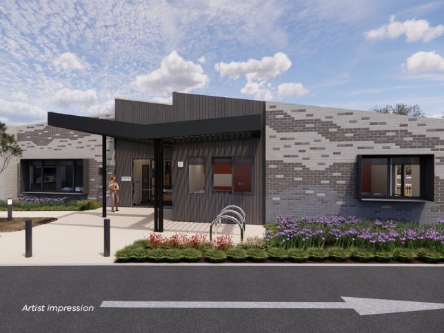 An artist's impression of a modern, single-story building with a mix of gray and brick-patterned walls. It features a black canopy over the entrance and decorative plants in front. Some individuals are near the entrance, and a bicycle rack is visible.