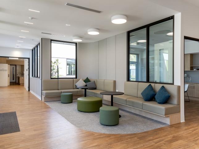 A modern interior area with large windows, neutral-toned seating and circular green ottomans next to some small tables.