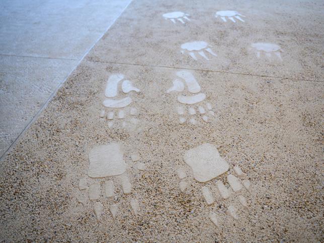 Footprint and track motifs embedded in a textured floor surface as part of an Indigenous wayfinding design.