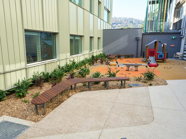 Children's outdoor play area with seating, native gardens and play equipment within a hospital courtyard.