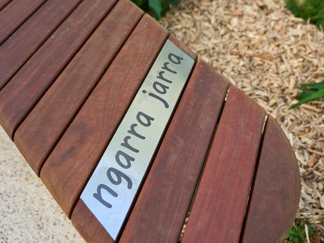 Close-up of a curved timber bench featuring the word "ngarra jarra" on a metal inlay.