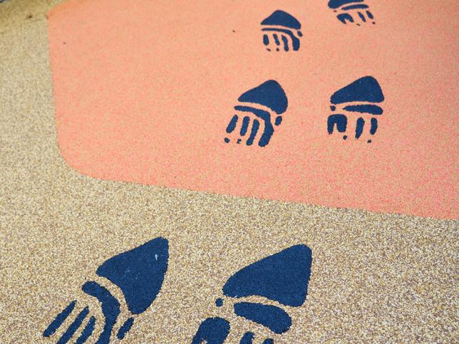 Indigenous footprint motifs incorporated into a coloured play surface in an outdoor courtyard.