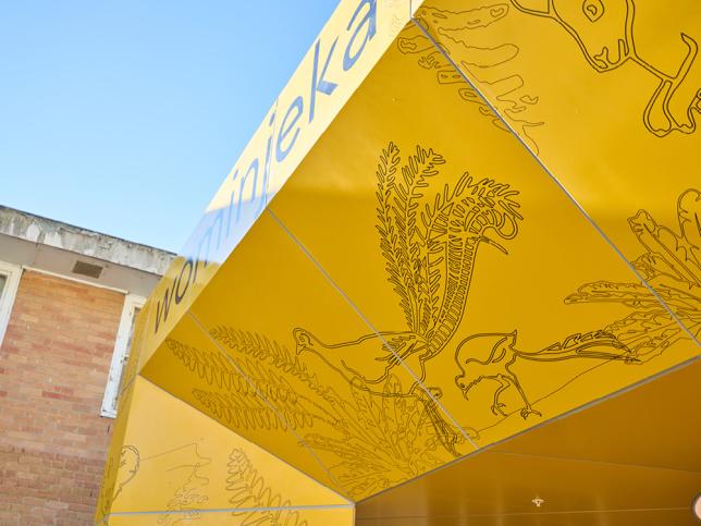 Detail of illustrated native birds and fern motifs on a yellow entrance canopy.