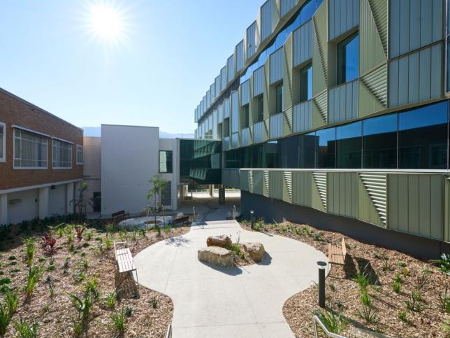 Landscaped courtyard at the new Angliss Hospital building, with a paved path, garden beds, timber seating and large rock features between two hospital wings.