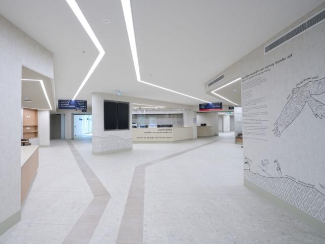 Main foyer at the new Angliss Hospital building, with wayfinding signs, a reception desk and Wurundjeri welcome artwork on the wall.