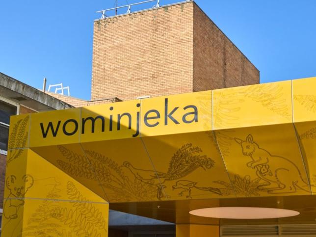 Yellow entrance canopy at the new Angliss Hospital building, featuring the word 'wominjeka' and line drawings of native plants and animals.