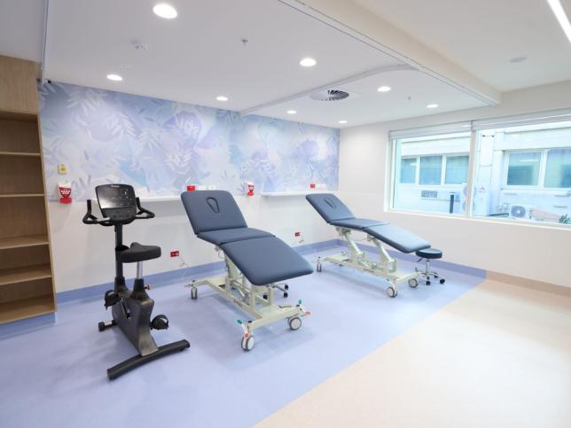 Outpatient therapy room at the new Angliss Hospital building, with treatment beds, an exercise bike and a mural of native plants on the wall.