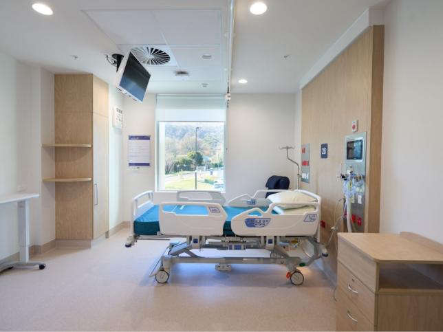 Single inpatient room at the new Angliss Hospital building, with a hospital bed, wall-mounted screen, built-in storage and a window with a garden view.