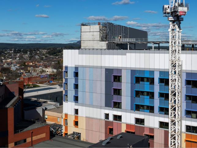 Exterior view of the Ballarat Base Hospital redevelopment showing a colourful multi-storey building under construction beside a tower crane.
