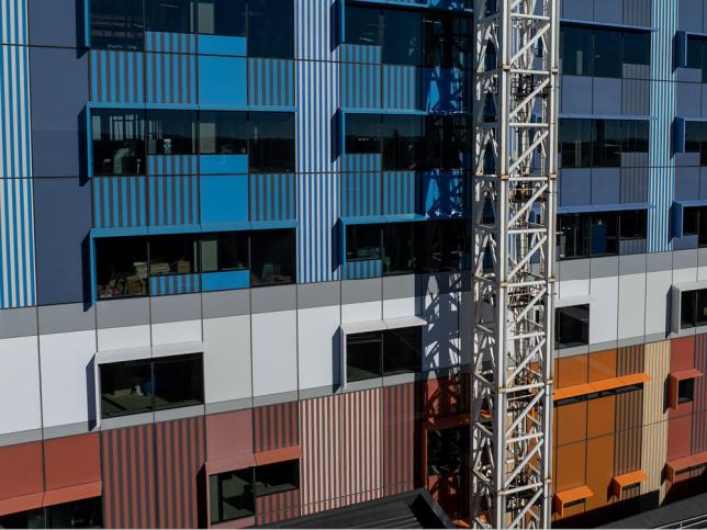 Close-up of the Ballarat Base Hospital redevelopment facade, featuring blue and grey cladding panels and a tower crane alongside the building.
