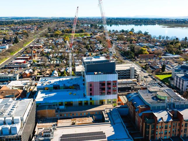 Aerial view of the Ballarat Base Hospital redevelopment construction site, with cranes, surrounding buildings and Lake Wendouree in the background.