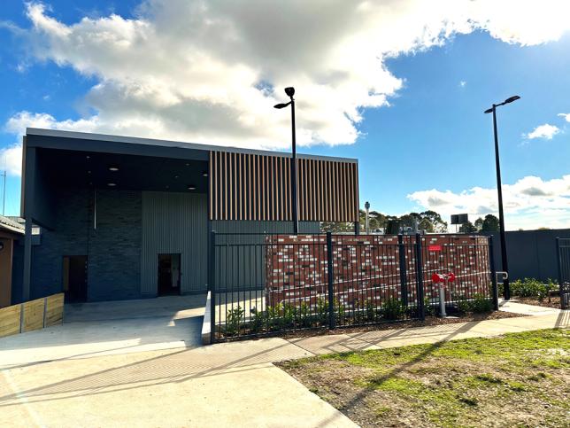 Modern building behind a black fence with a decorative brick wall and garden.