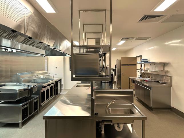 Commercial kitchen with stainless steel benches, sinks and cooking equipment.