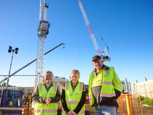 Three people in high-vis vests standing in front of two cranes