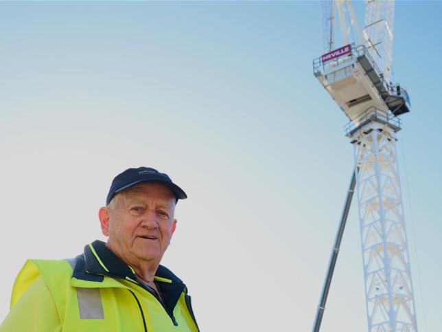 Crane honouree, Neville, standing in front of a crane