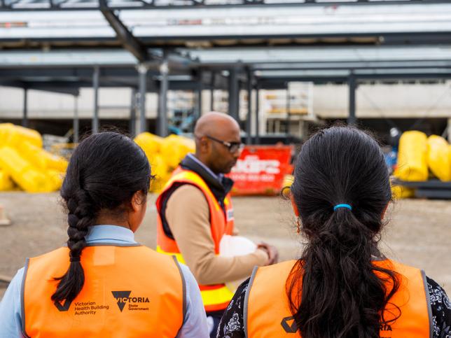 Two children and a man in high vis vests at a building site