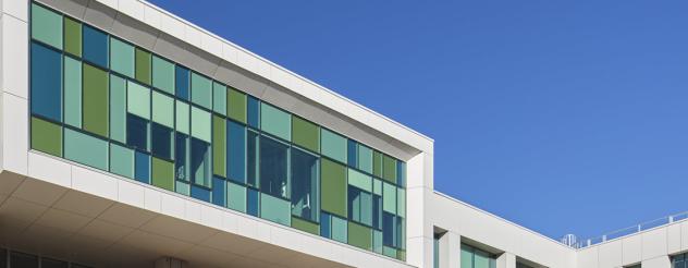 Photo looking up at top of modern building with coloured windows and clear sky