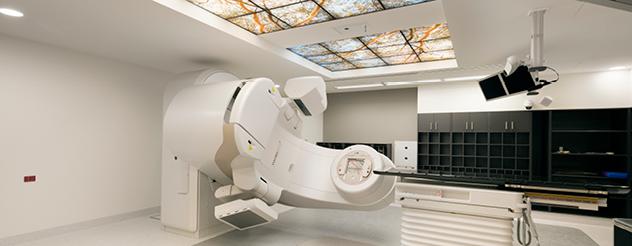 A white room with large medical equipment. There is a skylight with a view of trees.