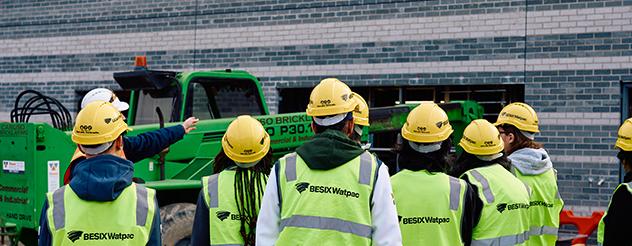A group of people from the back wearing construction hats and hi-vis